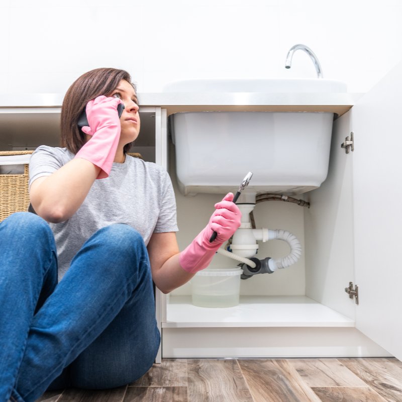 woman sitting near a leaking sink and calling a plumber