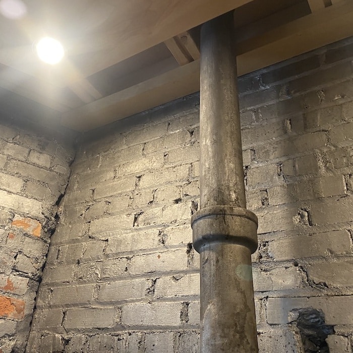 Cast iron pipe seen against exposed brick wall